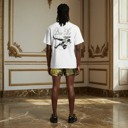 A model stands with their back to the camera in an ornate room with gold-trimmed cream walls and marble floors, wearing a white t-shirt with a black graphic print that says 'Give Me' and a cartoon character, paired with green and gold patterned shorts.